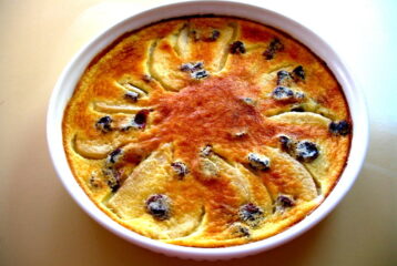 Pear and dried cherry clafouti in a round baking dish, dusted with confectioner’s sugar and photographed just after baking.
