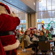 Auburn families enjoying a festive Breakfast With Santa event, with Santa greeting a cheering child in a decorated community hall.