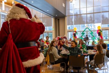 Auburn families enjoying a festive Breakfast With Santa event, with Santa greeting a cheering child in a decorated community hall.