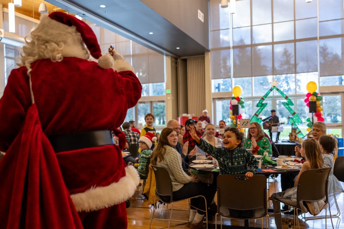 Auburn families enjoying a festive Breakfast With Santa event, with Santa greeting a cheering child in a decorated community hall.