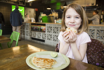 Little girls hold up quesadilla, smiling