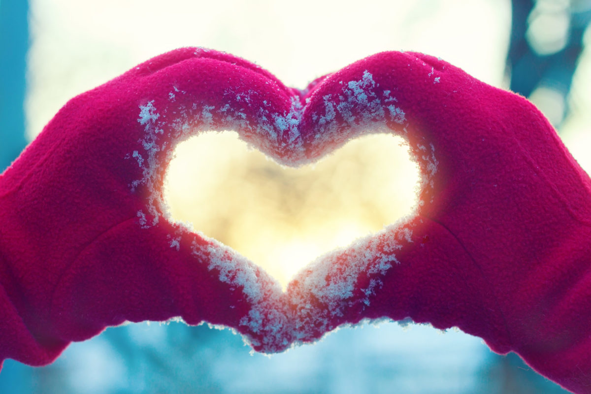 Red-gloved hands forming a heart shape in fresh snow, symbolizing holiday giving and community support.