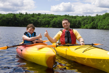 Parent and child kayaking together on a calm lake, wearing life jackets