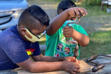 Day trip: boy helps his younger brother with a hand drill
