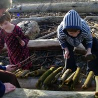 Play outside: grandmother watches two kids play with a xylophone made of kelp