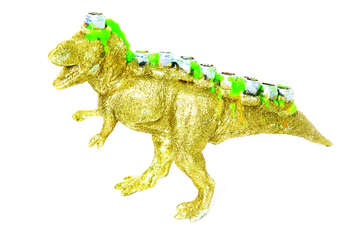 A handmade “Menorasaurus Rex” menorah — a bright, dinosaur-shaped hanukkiyah with candle holes along its back and big, toothy grin — ready for Hanukkah.