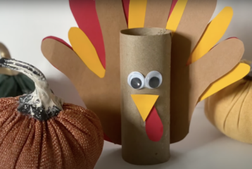 3-D Thanksgiving turkey craft made from a toilet paper roll with paper handprint feathers, googly eyes, and a small paper beak.