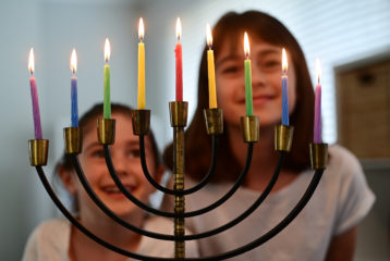 Smiling kids gather in front of a glowing menorah during a Chanukah celebration in Seattle.