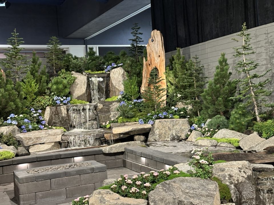 Stone slabs create a set with a waterfall, trees, and flowers at the Flower and Garden Festival in Seattle.