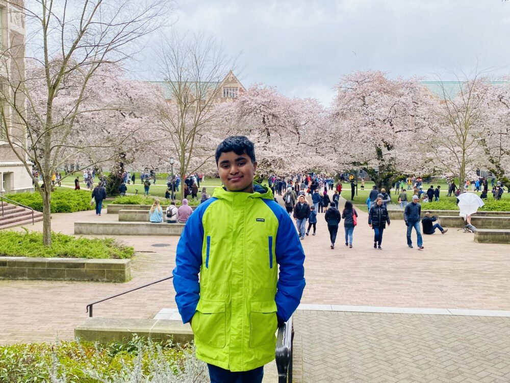 Boys stands in front of rows of cherry blossoms at the UW Quad