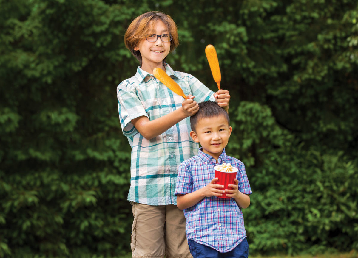 Two kids smiling and holding fair food at a summer fair
