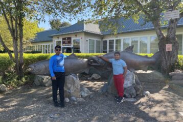 Two children stand in front of tall salmon statues at the Issaquah Salmon Hatchery.