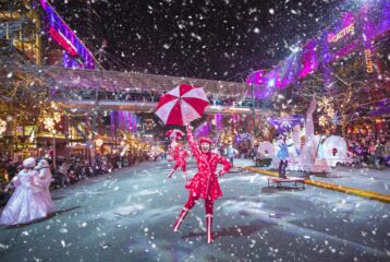 Snowflake Lane performer dancing along Bellevue Way in Bellevue, surrounded by lights, holiday decorations, and falling snow.