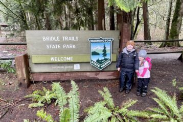 Two kids stand in front of state parks sign that says Bridle Trails