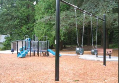 A toddler-friendly playground in Bellingham, featuring wooden play structures, small slides, and a fenced area surrounded by trees for safety and family fun.