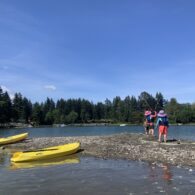 Two kids playing on a beach near colorful kayaks during a family paddling outing