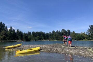 Two kids playing on a beach near colorful kayaks during a family paddling outing