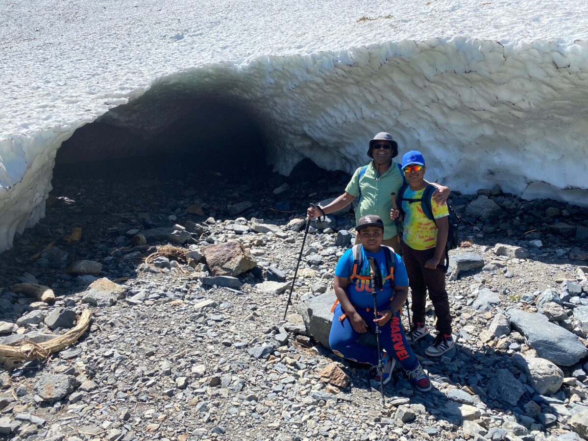 Family standing in front of the Big Four Ice Caves, with large snow formations and rocky terrain visible in the background.