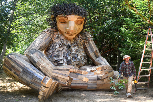 Artists Thomas Dambo walks away from the giant troll that seated cross-legged.
