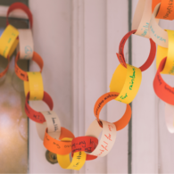 Close-up of a colorful paper “thankful chain” with handwritten gratitude messages linked together and draped across a living room shelf.