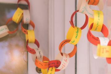 Close-up of a colorful paper “thankful chain” with handwritten gratitude messages linked together and draped across a living room shelf.