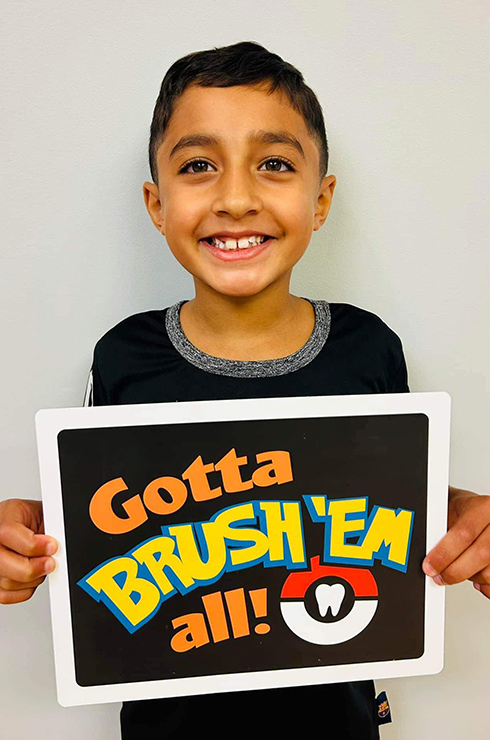 Smiling child holding sign that says "Gotta Brush 'Em All"