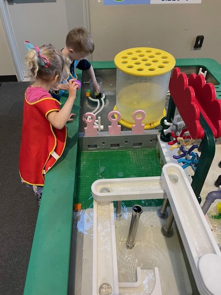 Kids play at a water table, wearing waterproof vests.