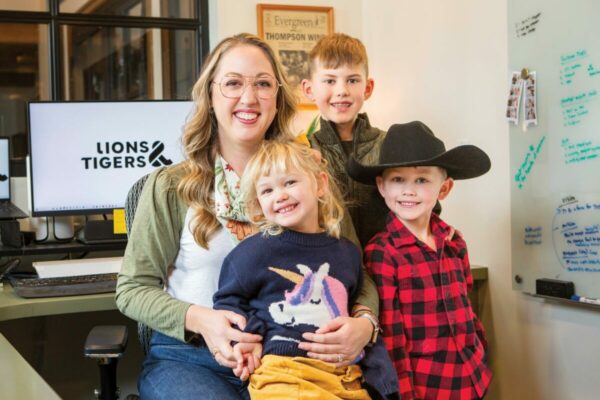 Woman sits at office desk with computer in the background, surrounded by three child.