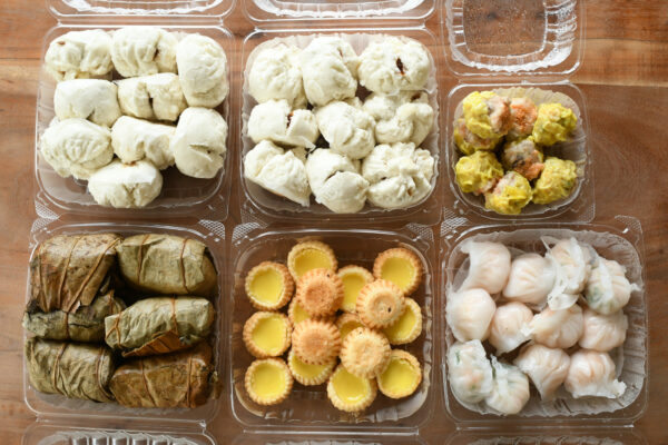 Six open takeout containers filled with various dim sum items sitting on a table, shot from above.