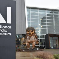 Exterior shot of the National Nordic Museum, with the museum's sign in frame, building in the distance, and giant troll made up of recycled materials right in front.