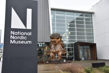 Exterior shot of the National Nordic Museum, with the museum's sign in frame, building in the distance, and giant troll made up of recycled materials right in front.