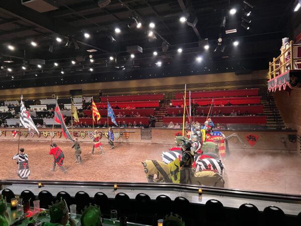 Interior of Medieval Times, showing knights dressed up in full gear atop horses, behind flag bearers ready to joust.