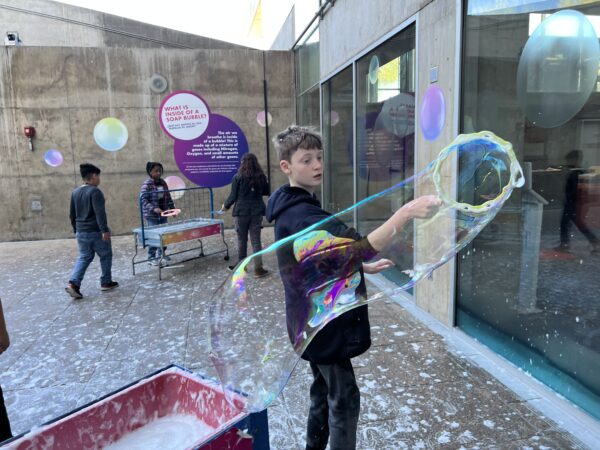 Young boy in motion making a large bubble at the Children's Museum.