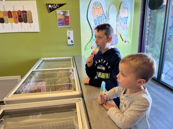 Two boys eating popsicles at a counter.