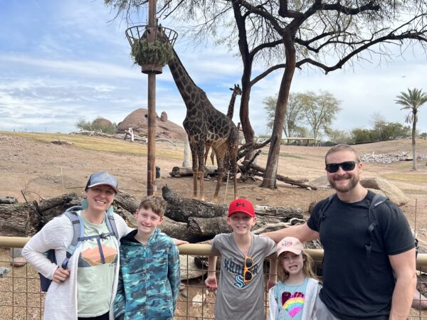Family posing for a photo in front of two giraffes at the zoo.