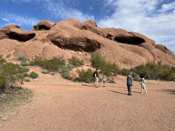 Kids and adults in front of large desert rock formation.