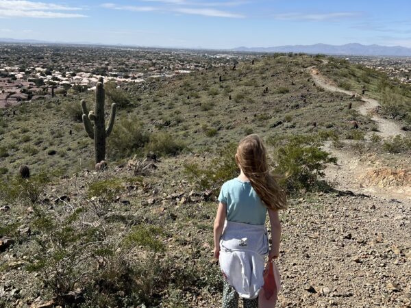 Young girl looks out at desert landscape, under blue skies.