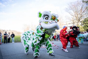 Green and white lion participate in traditional Lion Dance in street, onlookers line street watching.