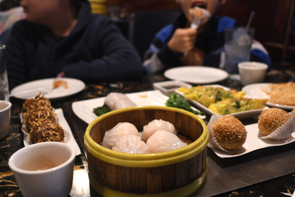 Dim sum items like pork buns, dumplings, potstickers, and sesame balls are scattered across a table.