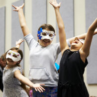 Three kids in Phantom of the Opera-style masks wave their hands in delight
