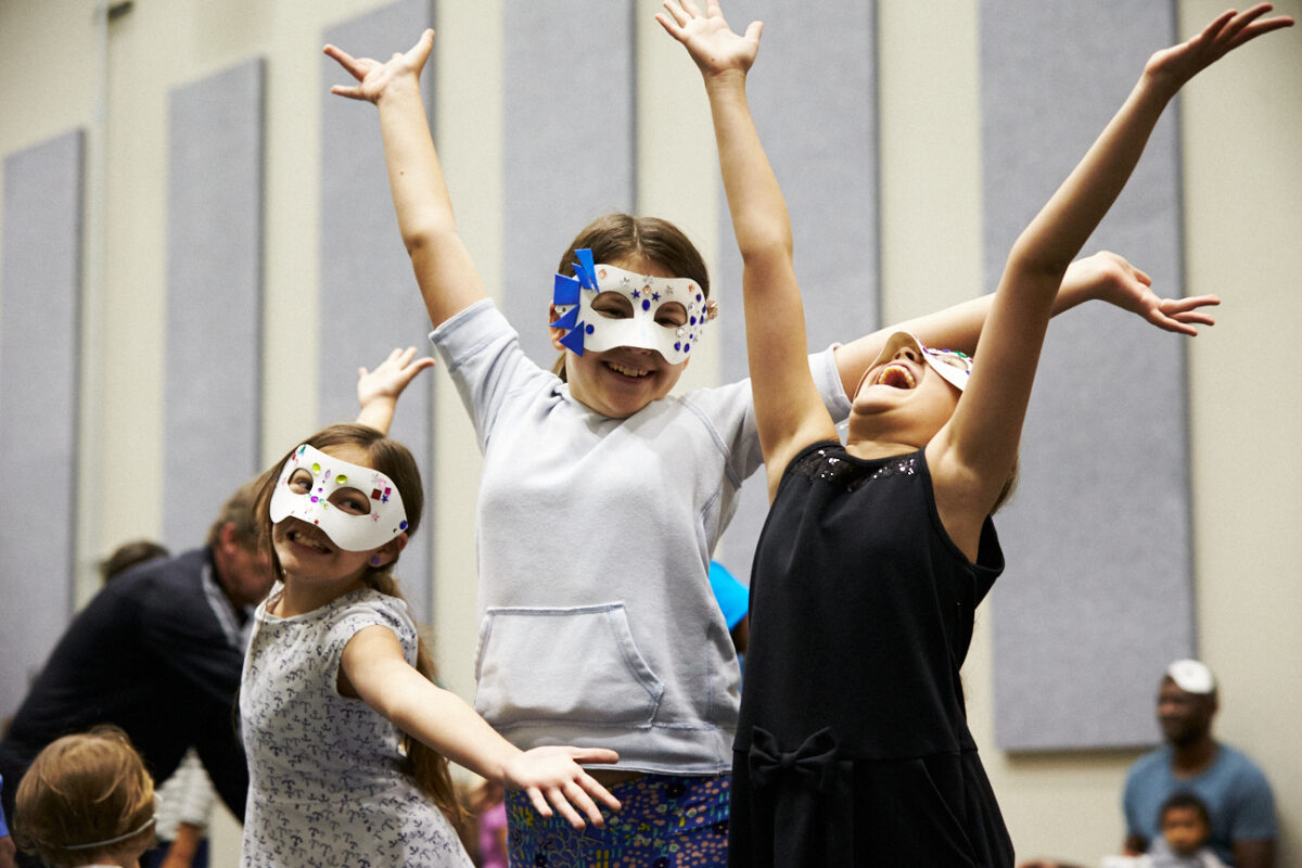 Three kids in Phantom of the Opera-style masks wave their hands in delight