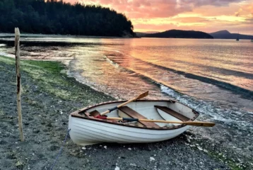 Row boat is moored on the beach, with a gorgeous orange and yellow sunset behind it against the water.