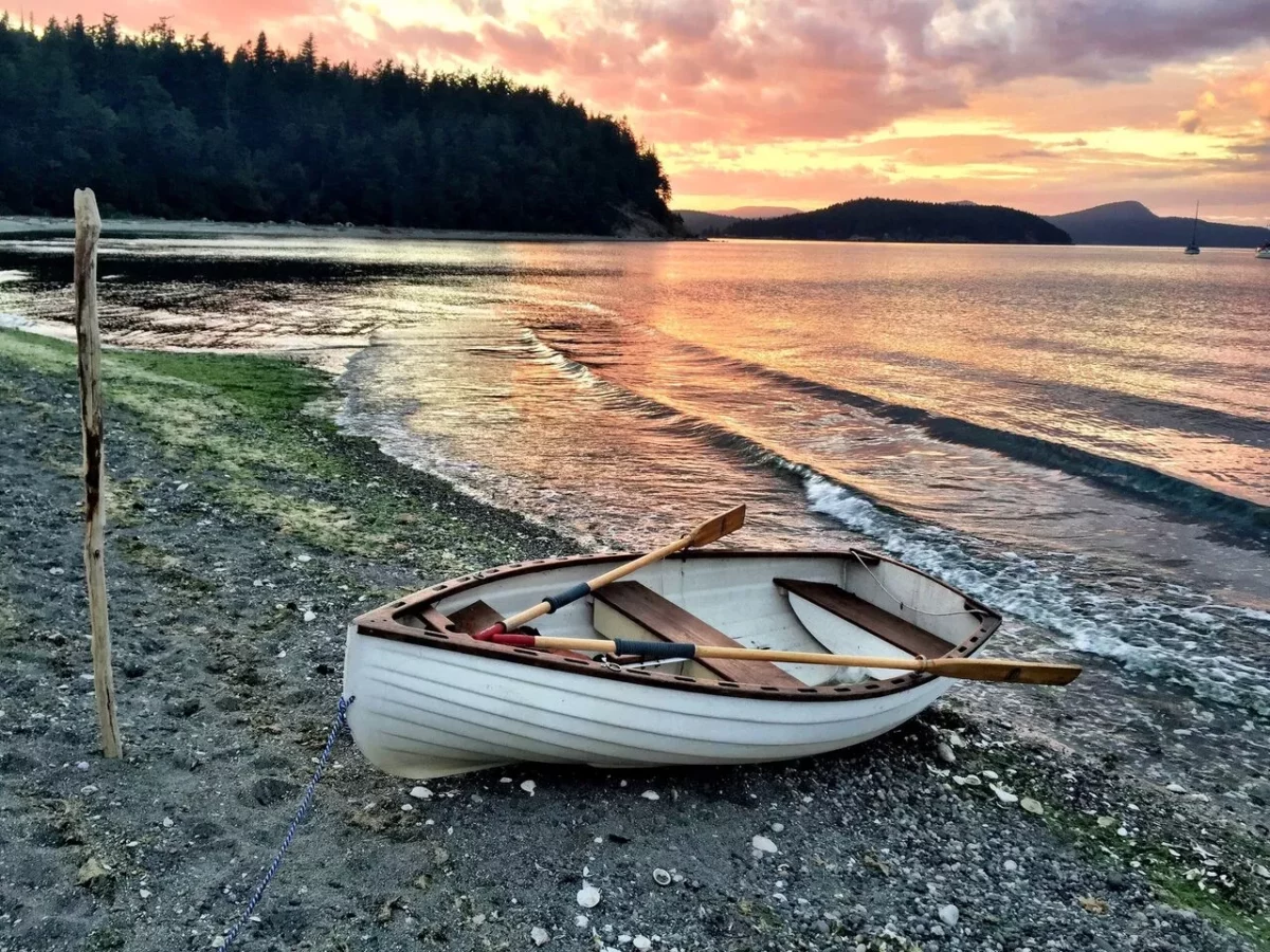 Row boat is moored on the beach, with a gorgeous orange and yellow sunset behind it against the water.