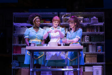 Three actresses in waitress uniforms stand baking a pie