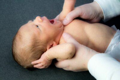Newborn yawning, with adult hands hold it's cheest