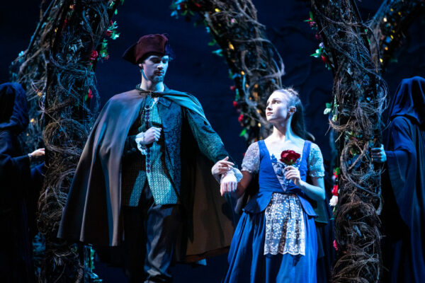 Female and male dancers hold hands on stage, female dancer holds a rose