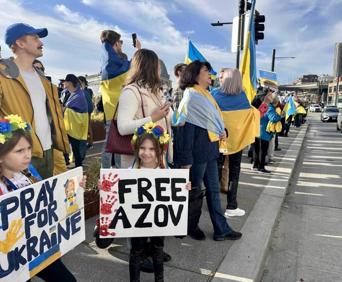 Kids and adults in blue and yellow hold signs in support of Ukraine.