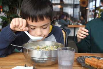Kid sits at a table eating a bowl of pho