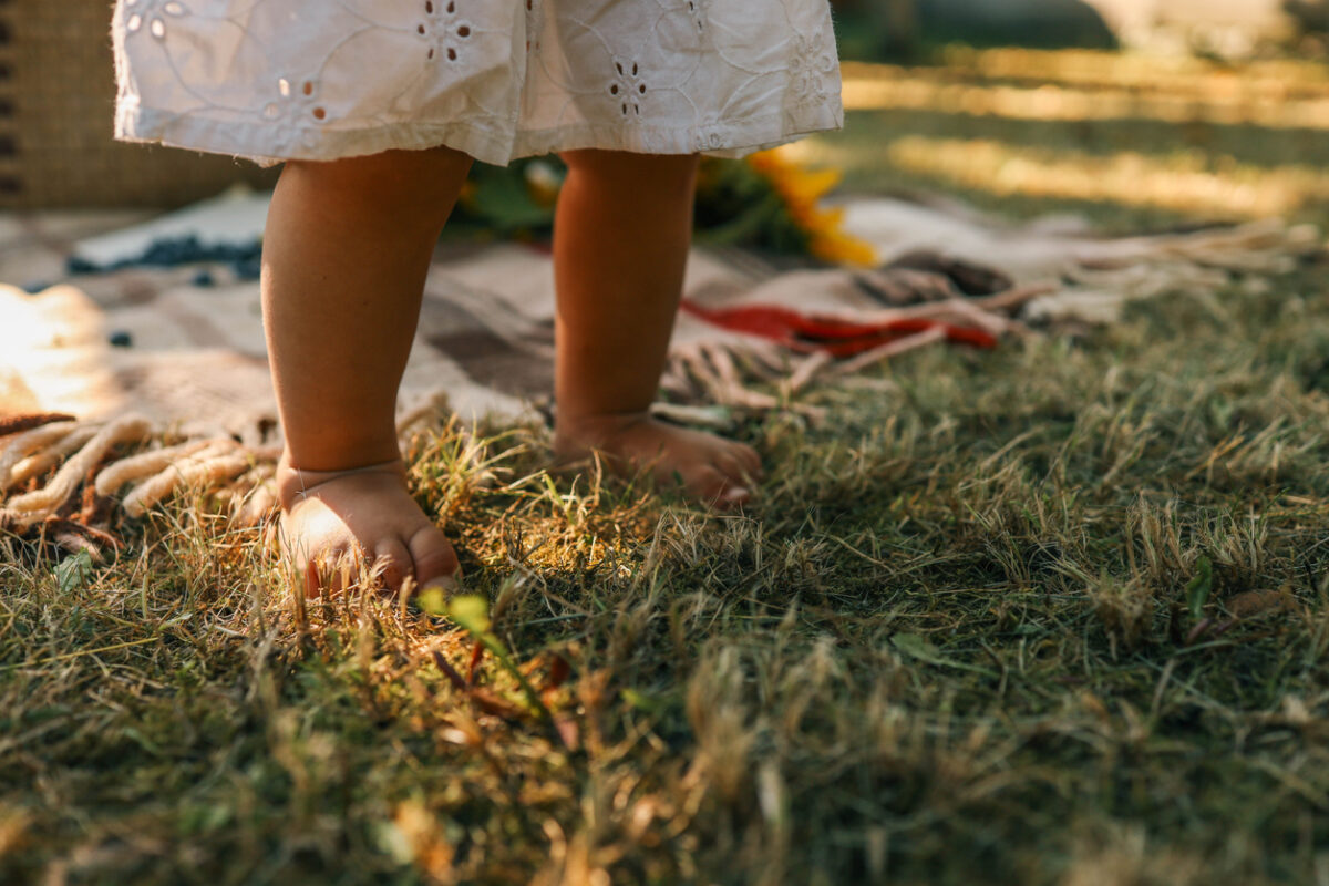 Little child walking on green grass outdoors, closeup.
