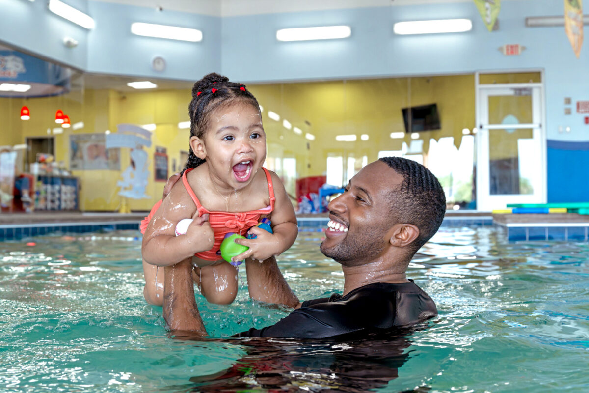 Adult holds smiling child up in pool